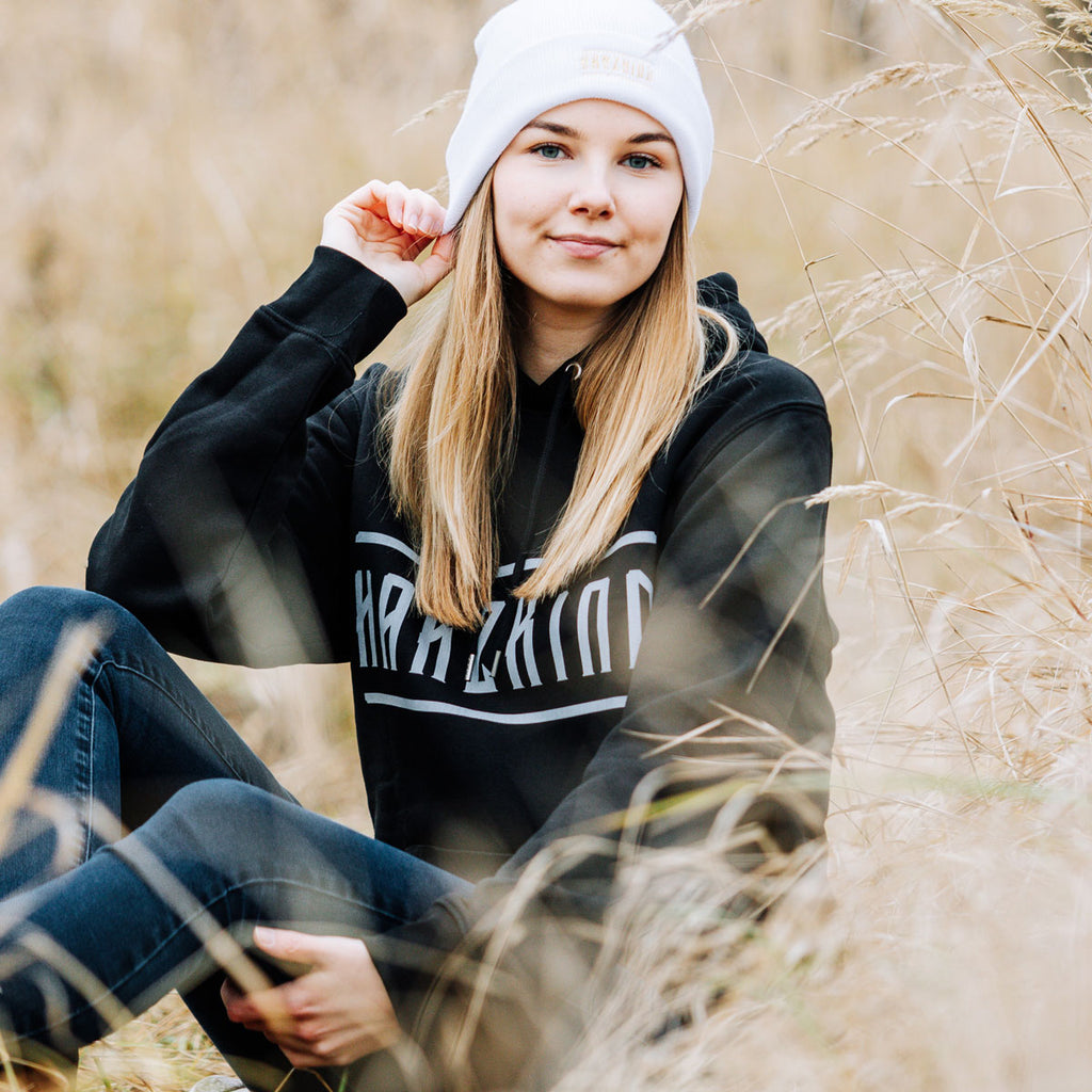 Weibliches Model mit schwarzem Harz Hoodie mit weißem HARZKIND Logo – nachhaltig, Fair Wear & OEKO-TEX, pro Kauf 1 Baum im Harz